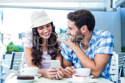 Cute couple sitting in cafe looking at smartphone