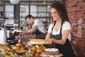 Smiling waitress holding cake in front of colleague