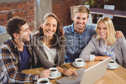 Smiling friends drinking coffee and using laptop