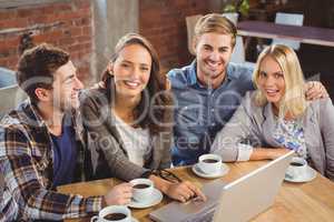 Smiling friends drinking coffee and using laptop