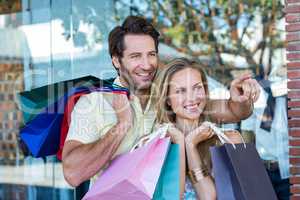 Smiling couple with shopping bags looking and pointing