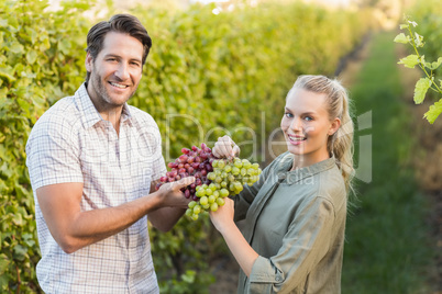 Two young happy vintners holding grapes