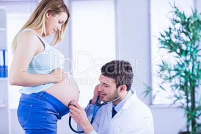 Smiling doctor examining stomach of standing pregnant patient