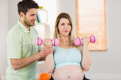Pregnant woman sitting on exercise ball and lifting dumbbells