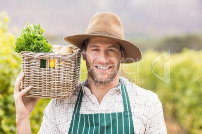 Young happy farmer holding a basket of vegetables