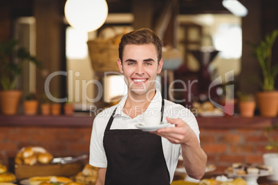 Smiling barista offering cup of coffee to camera