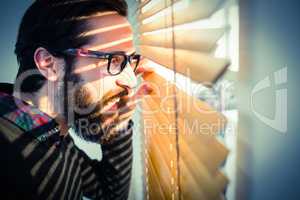Hipster businessman peeking through blinds