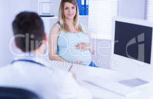 Smiling pregnant patient looking at camera while doctor taking n
