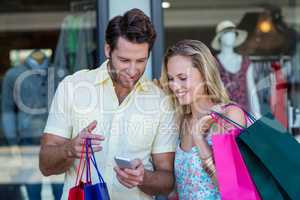 Smiling couple with shopping bags looking at smartphone