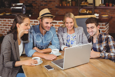 Smiling friends drinking coffee and using laptop