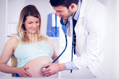 Smiling doctor examining stomach of pregnant patient