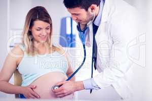 Smiling doctor examining stomach of pregnant patient
