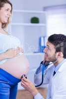 Smiling doctor examining stomach of standing pregnant patient