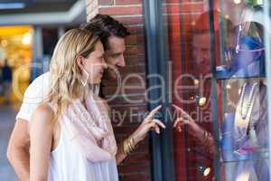 Smiling couple going window shopping and pointing at necklaces