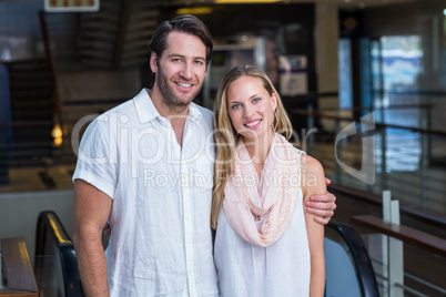 Smiling couple putting arms around in front of escalator