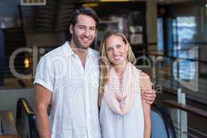 Smiling couple putting arms around in front of escalator