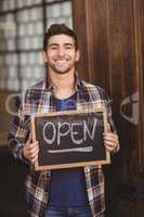 Smiling casual waiter showing chalkboard with open sign