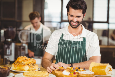 Smiling waiter tidying up the pastries