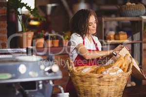 Smiling waitress putting bread in a paper bag
