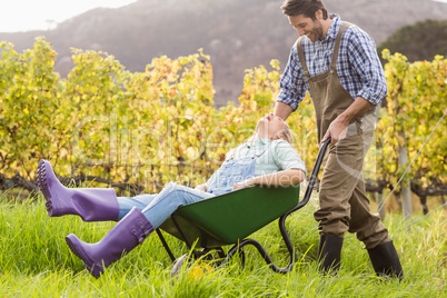 Laughing couple in dungarees pushing a wheelbarrow