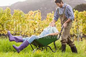 Laughing couple in dungarees pushing a wheelbarrow