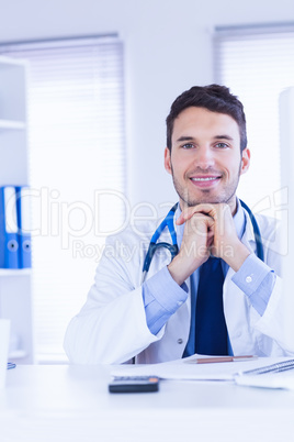 Portrait of smiling doctor looking at camera with hands folded