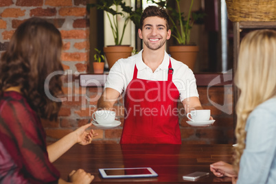 Smiling waiter serving coffees to customers