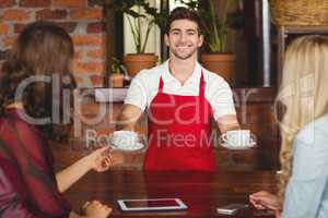 Smiling waiter serving coffees to customers