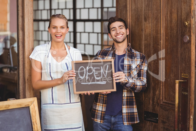 Smiling waitress and man holding chalkboard with open sign