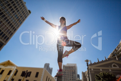 Athletic woman balancing on bollard and stretching out her arms