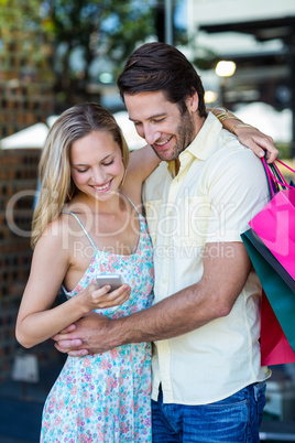 Smiling couple embracing and looking at smartphone