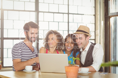 Smiling friends looking at laptop and having coffee