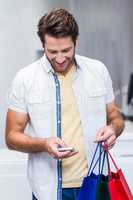 Smiling man with shopping bags using smartphone