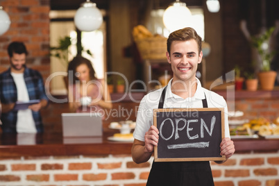 Smiling barista holding chalkboard with open sign