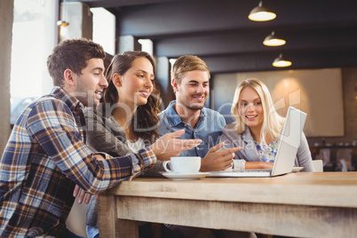 Smiling friends drinking coffee and pointing on laptop screen