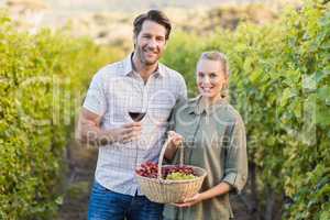Two young happy vintners holding a basket of grapes and a glass