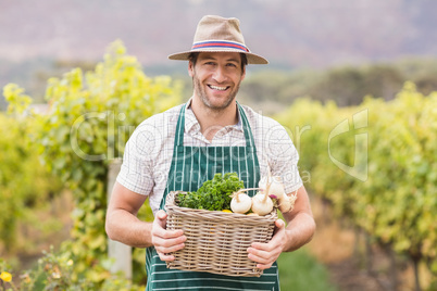 Young happy farmer holding a basket of vegetables