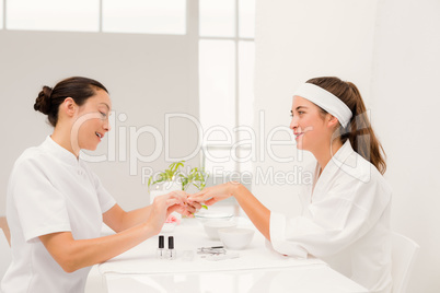 Beautiful woman with beautician applying nail varnish to female
