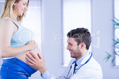 Smiling doctor checking stomach of standing pregnant patient