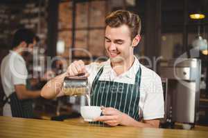 Smiling barista pouring milk in a cup