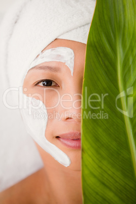 Attractive woman with cream treatment behind a leaf