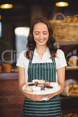 Pretty waitress showing a plate of cupcakes