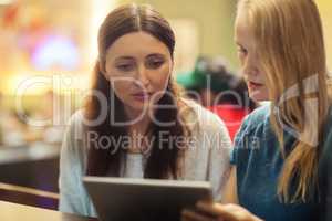 Two women have a discussion in the restaurant using electronic tablet