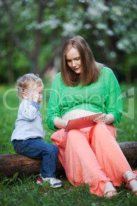 Pregnant mother with little son using touch pad in the park