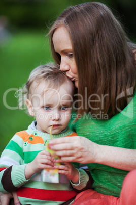 Mother kissing the child drinking juice outdoor