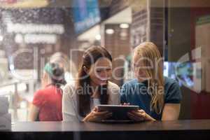 Two women talk cheerfully in the restaurant using electronic tablet