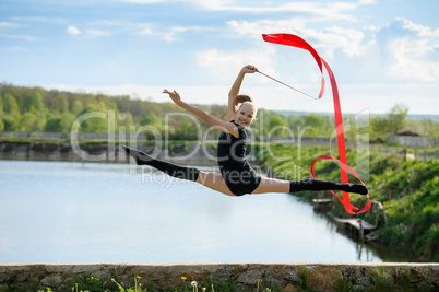 Gymnast girl doing leg-split in a jump with ribbon