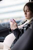 Pregnant woman texting on cell in the car