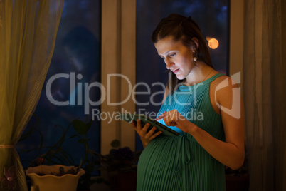 Pregnant woman using tablet in the evening