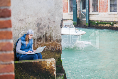 Young woman using laptop by the canal in Venice